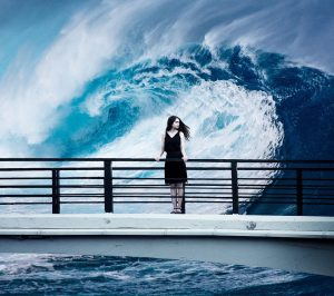 junge Frau steht auf einer Brücke am Meer, hinter ihr i9st eine riseige Welle zu sehen, Credit: Sarah Richter, Pixabay