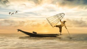Balancierender Fischer auf Fischerboot im Sonnenuntergang